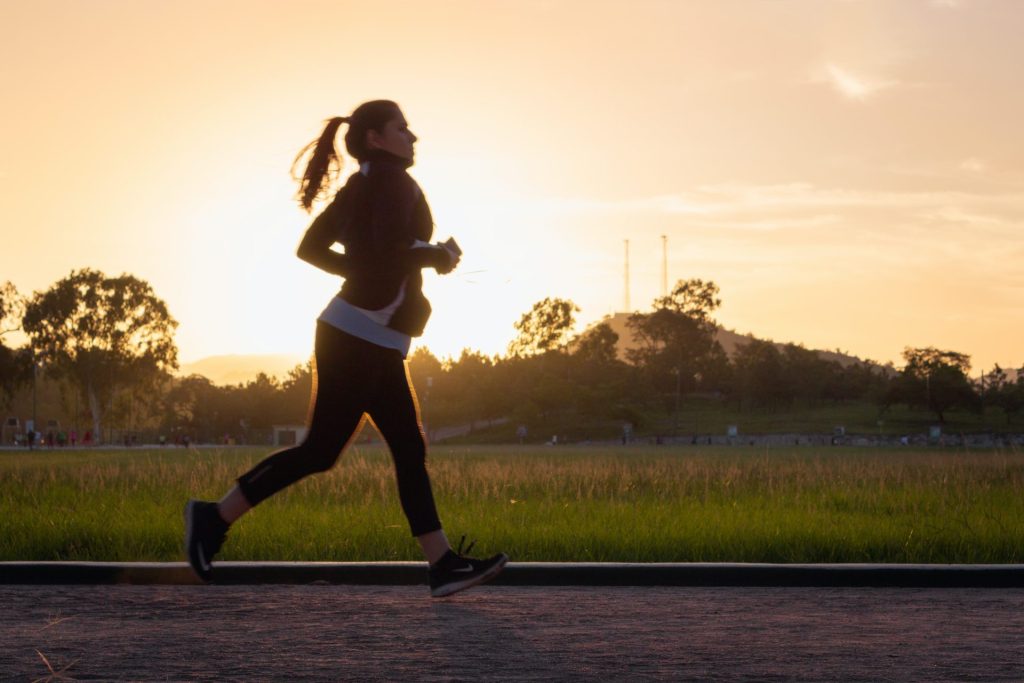A woman running during a beautiful sunset, representing the study's findings on the relationship between regular exercise, enhanced macrophage function, and potential longevity