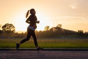 A woman running during a beautiful sunset, representing the study's findings on the relationship between regular exercise, enhanced macrophage function, and potential longevity
