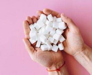 An image depicting a lady holding several sugar cubes in her hands, symbolizing the concept of hidden sugars in our everyday foods and beverages