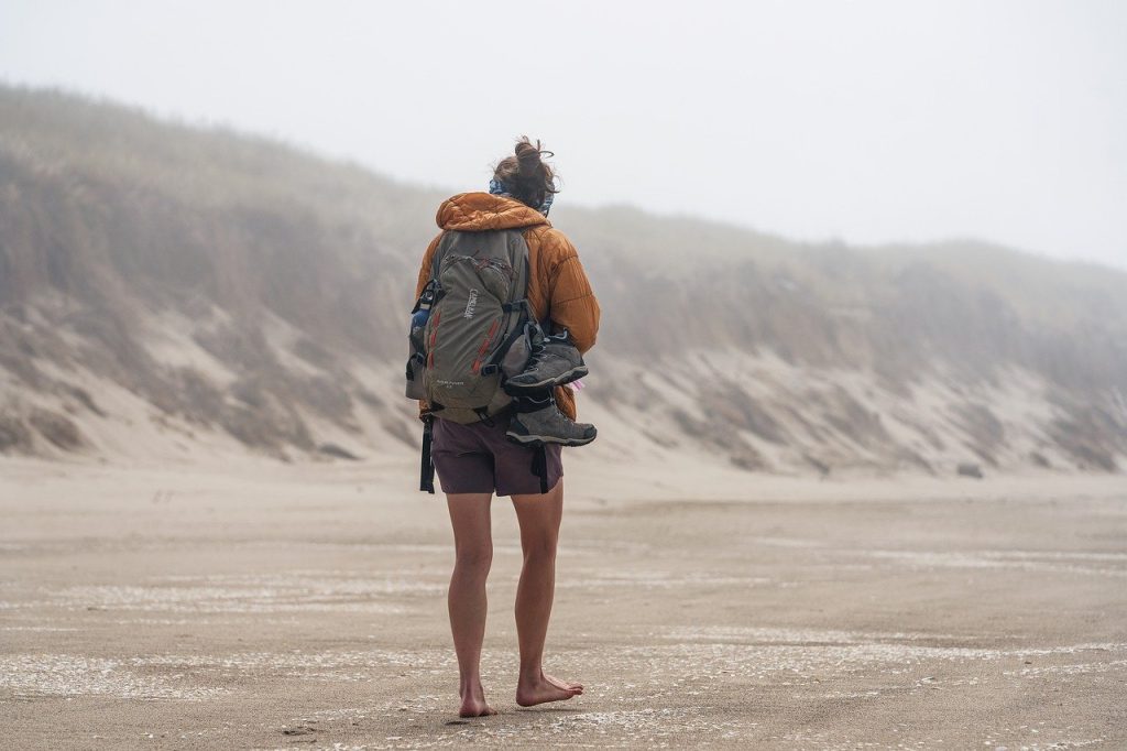 Image captures a serene moment of barefoot walking: a woman on a beach.